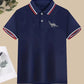 Chemise polo garçon bleu marine à col tricolore et motif dinosaure – tenue élégante et décontractée