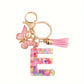 Porte-clés femme lettre initiale colorée – Breloque papillon et pompon rose tendance